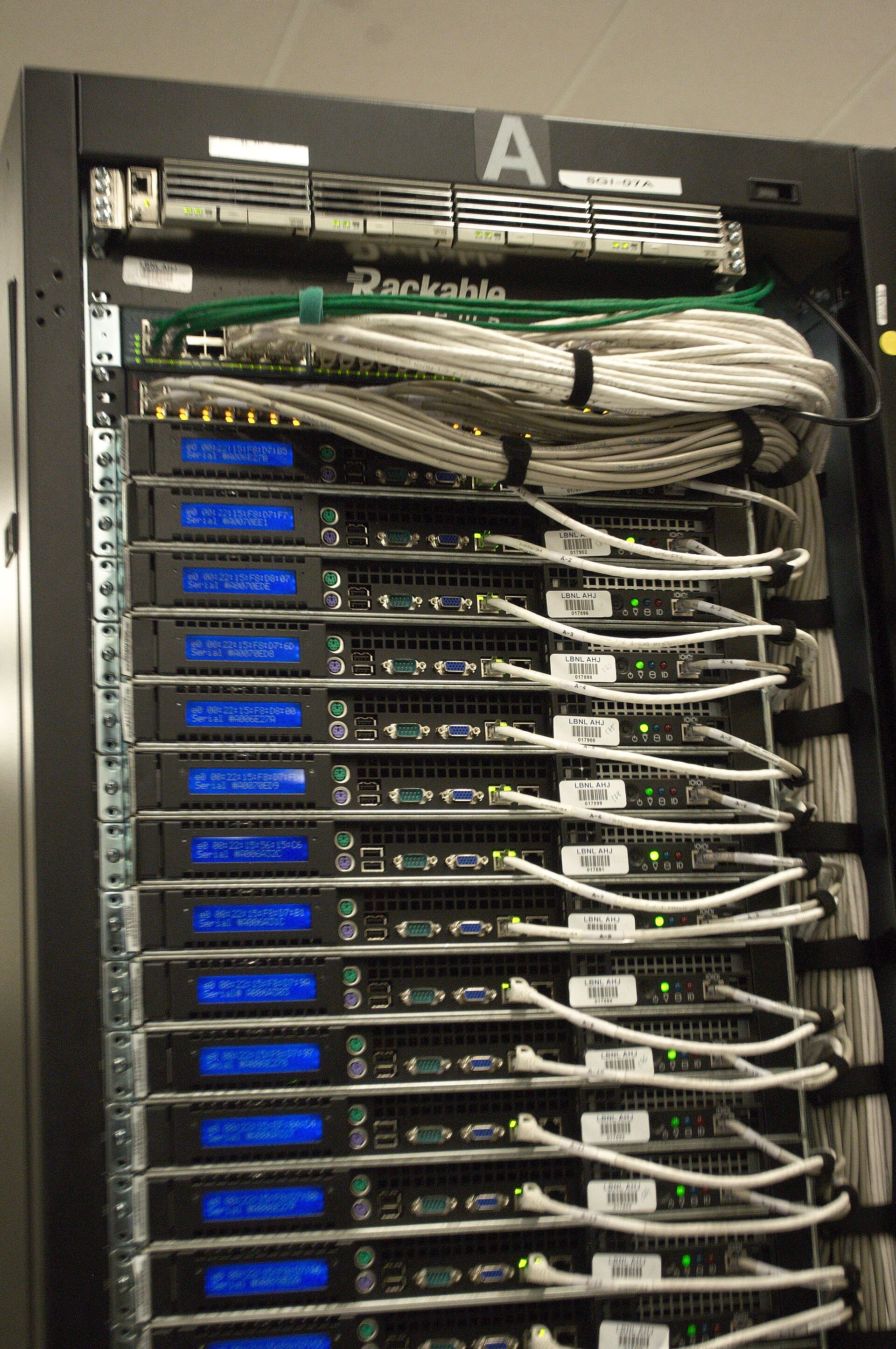 The back of a server rack: a column of 1U servers with blue serial-number screens, green status lights and bundled white network cables.